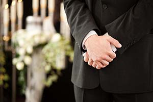 Mies kädet ristissä hautajaisissa.