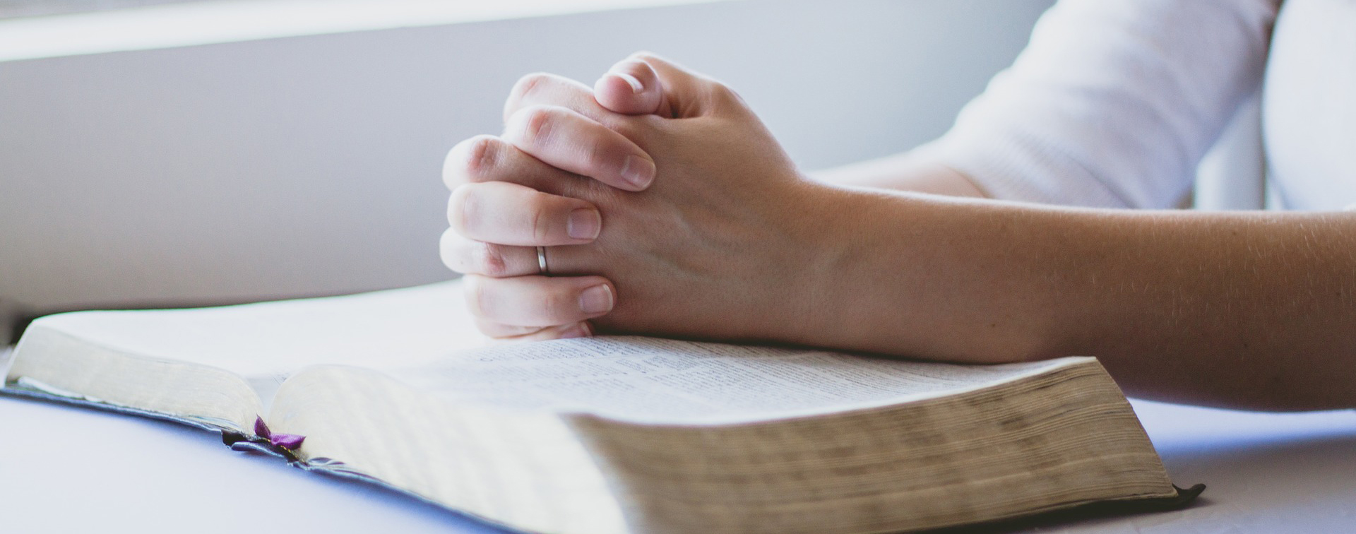 Naisen kädet rukouksessa Raamatun päällä.