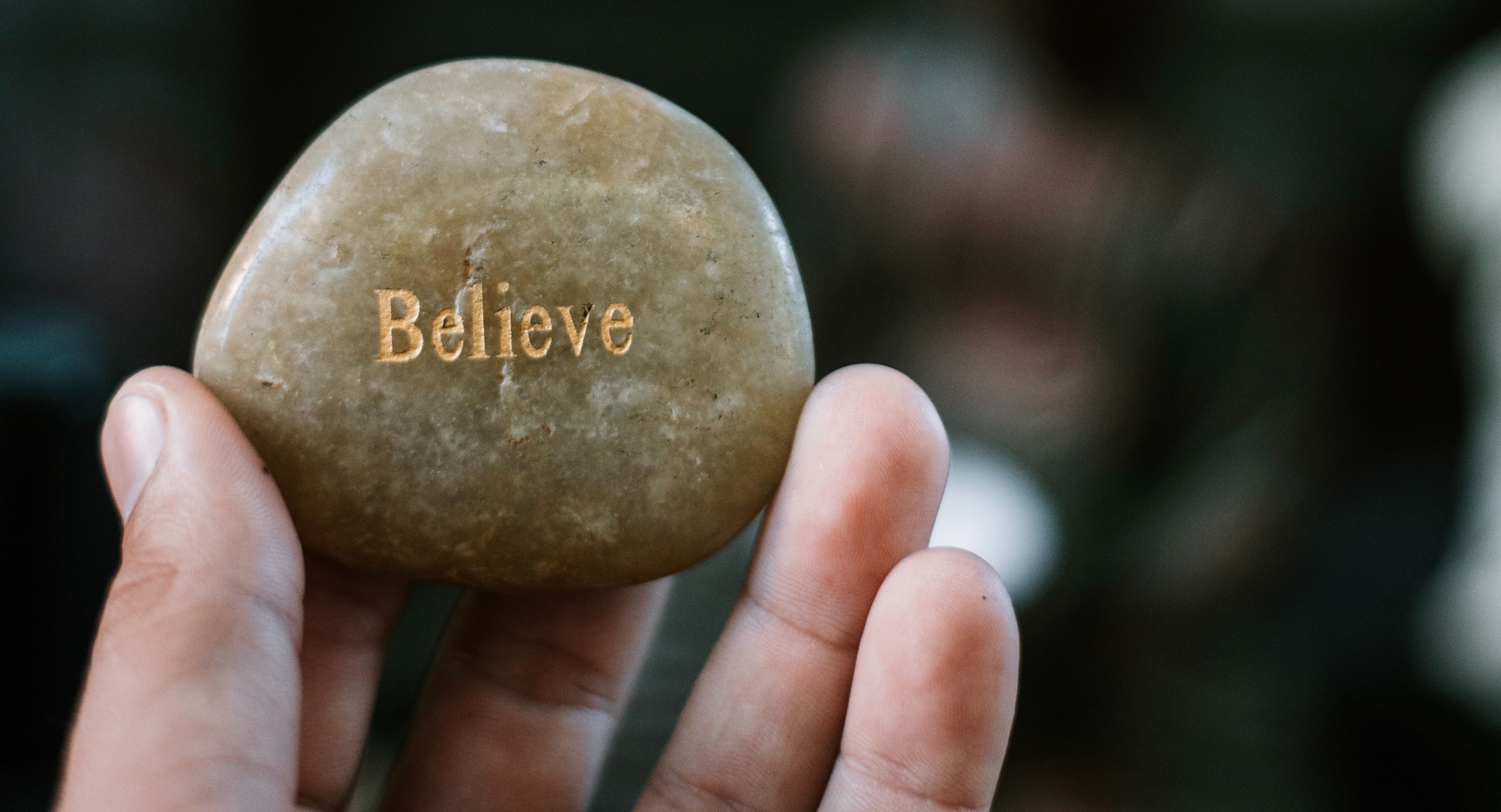 Miehellä on kädessään kivi, jossa lukee Believe, suomeksi usko.