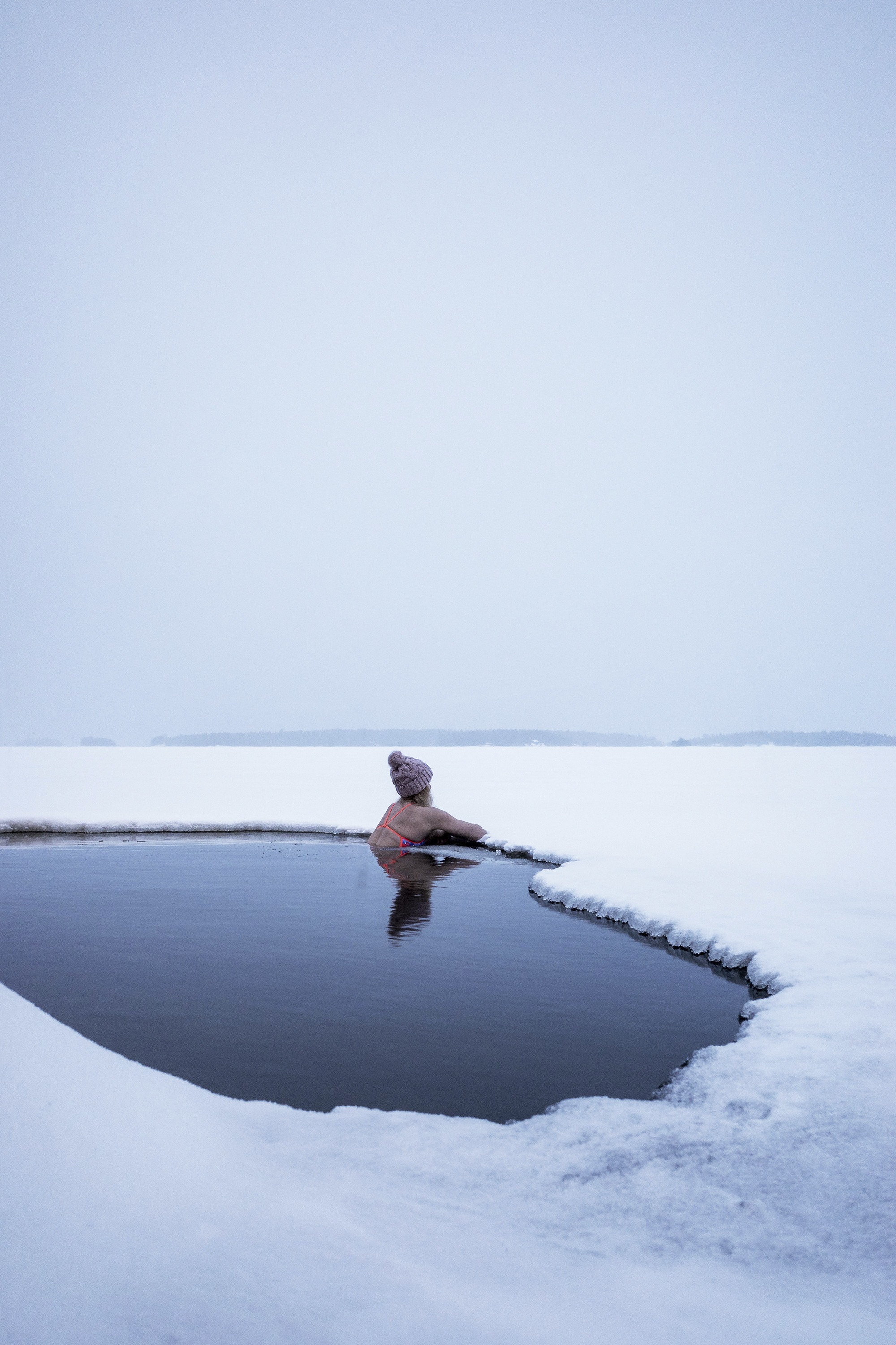 Nainen avannossa katselee talvista järvimaisemaa.