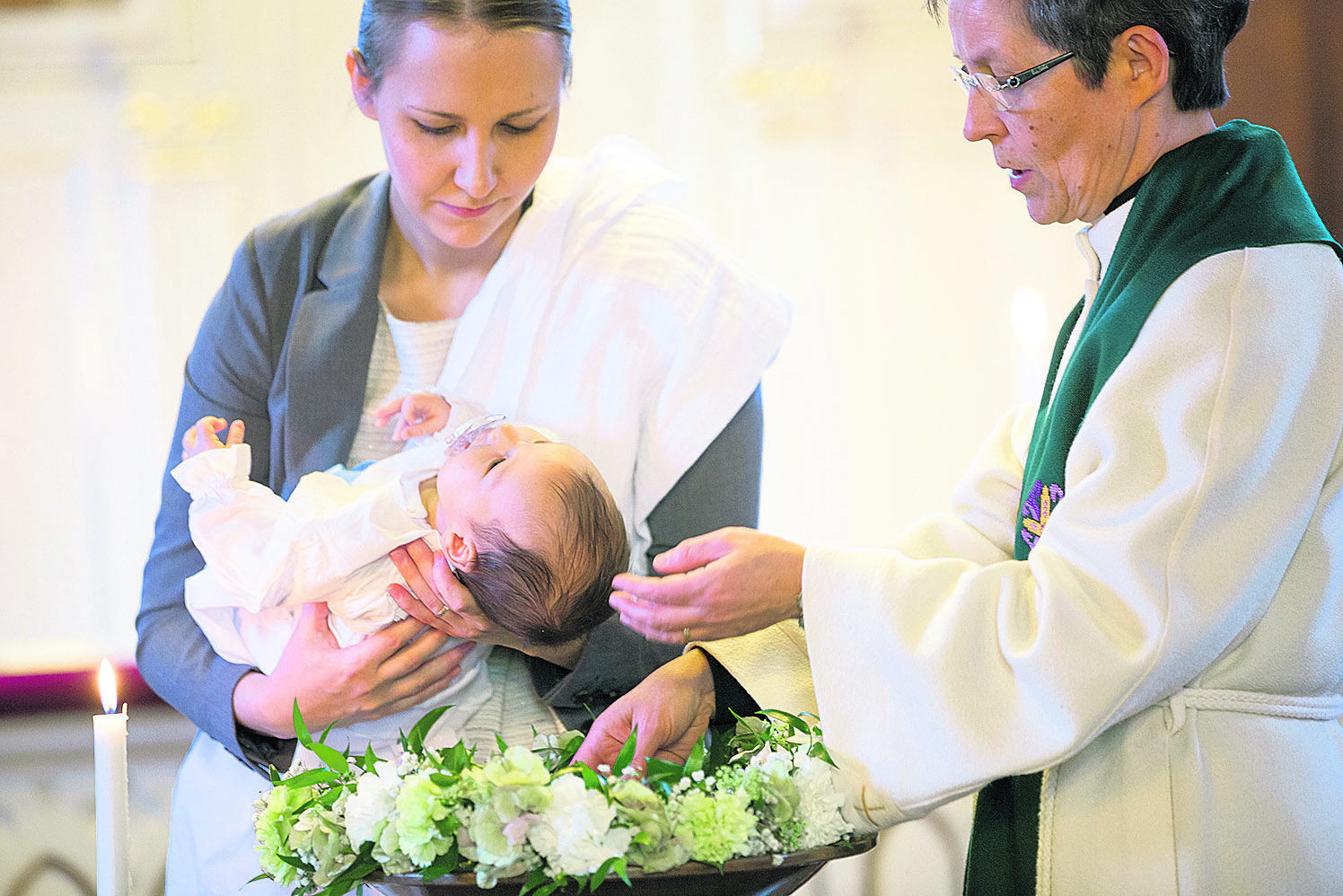Vauva kummin sylissä, pappi kastaa.