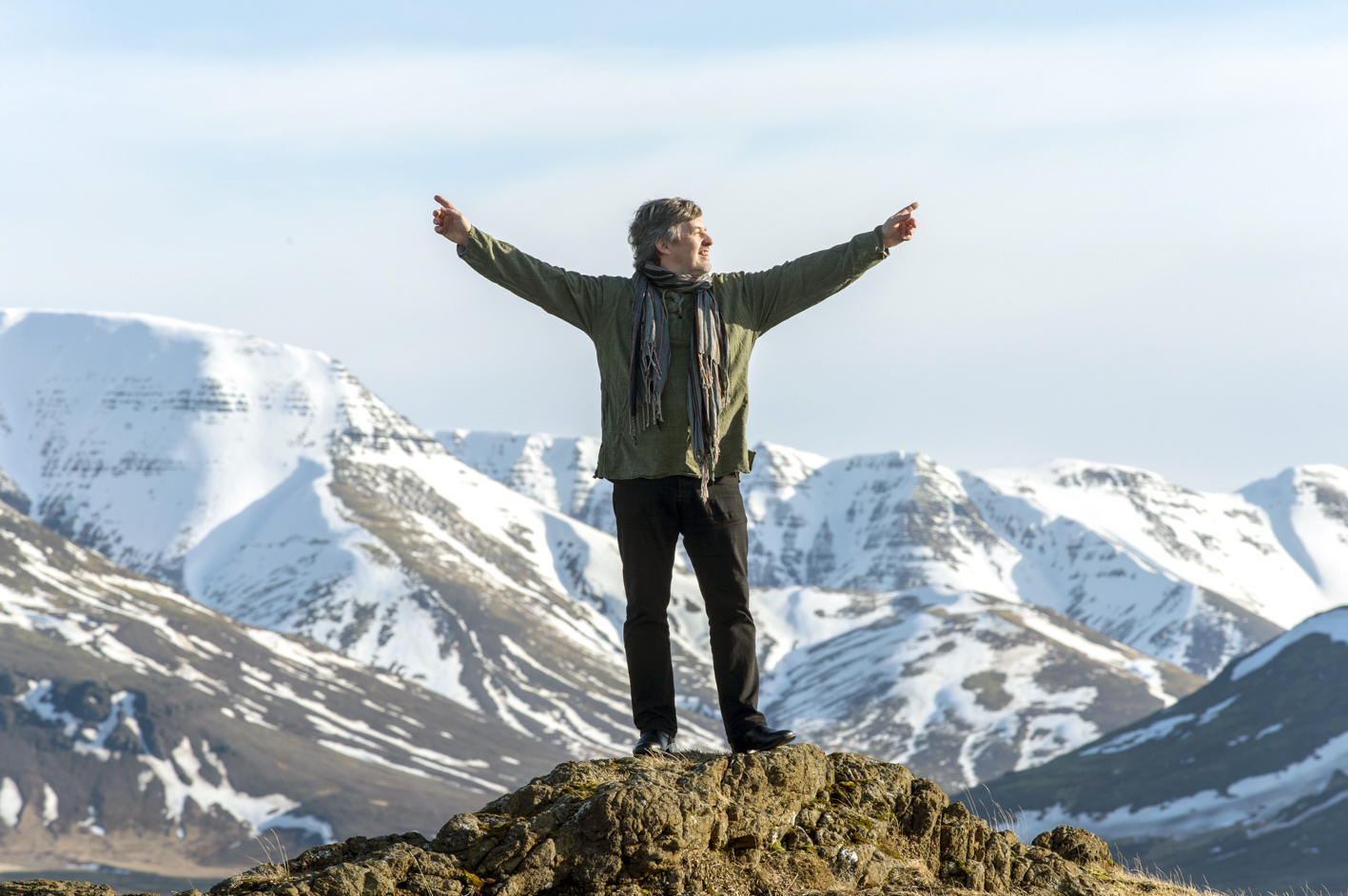 Pekka Simojoki seisoo vuoren laella kädet ylhäällä.