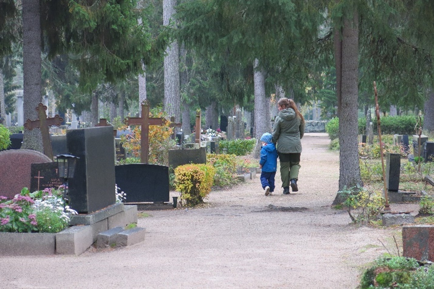 Aikuinen ja lapsi kävelevät Marian hautausmaalla ja katselevat hautakiviä..